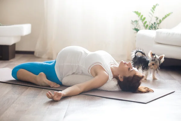 Pregnant woman and her pet dog doing yoga at home