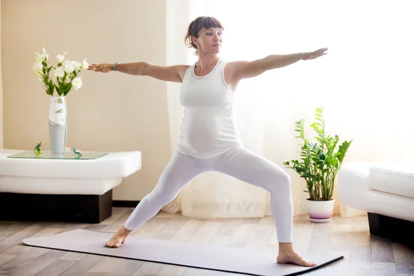 Pregnant woman doing Warrior Two yoga pose at home