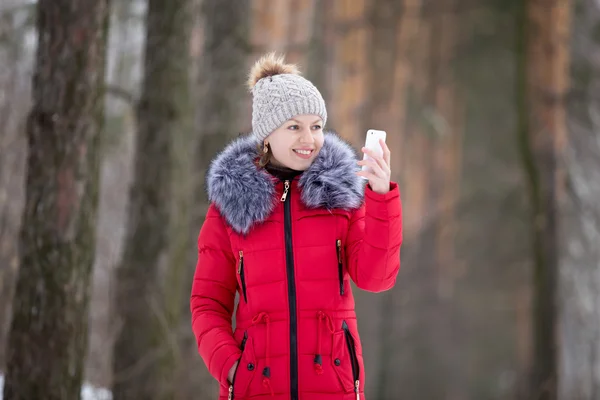Happy smiling female in red winter jacket looks on her mobile ph
