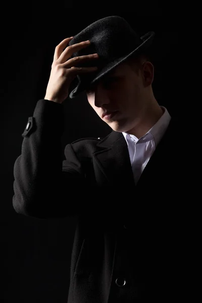 Handsome mafioso man touching hat in the dark
