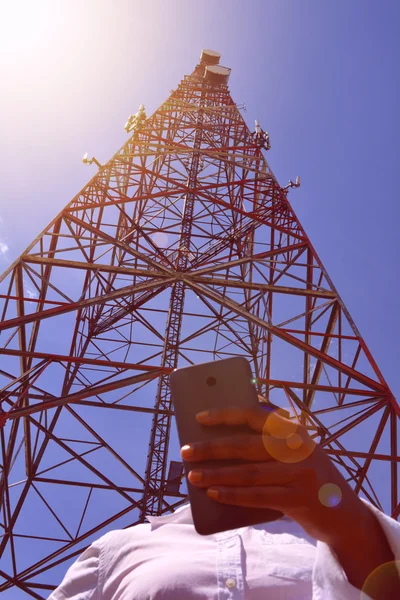Woman holding a smartphone near telecommunication tower