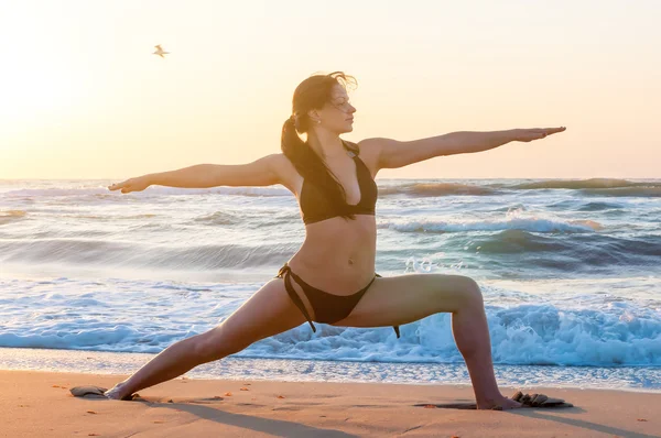 Woman practicing Warrior yoga pose outdoors over sunset sky background