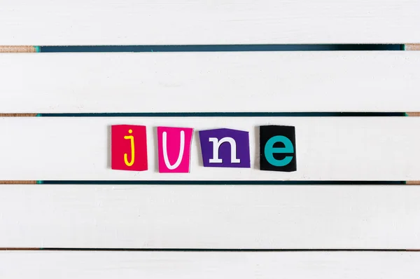 June written with color magazine letter clippings on white wooden board. Summer vacation concept