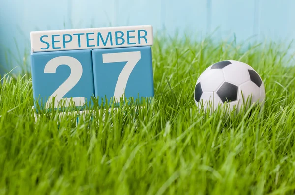 September 27th. Day 27 of month, wooden color calendar on green grass lawn background. Autumn time. Empty space for text