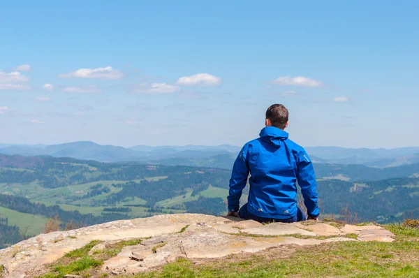Man, traveler sitting on the edge of a cliff and watching peaceful landscape.