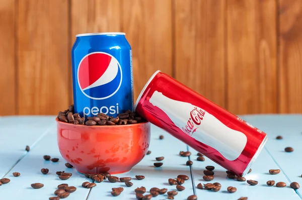 Kiev, Ukraine, April 2015. Can Pepsi cola in a bowl of coffee standing on blue table and fallen Coca-Cola, dark wooden background with empty space. Marketing Warfare two corporations. Unhealthy drinks