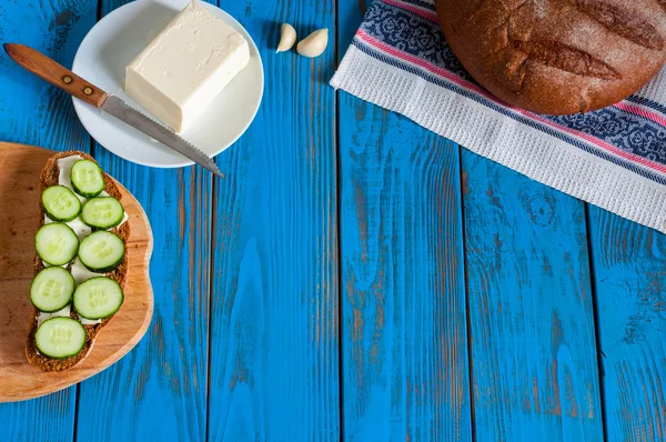 Freshly baked bread, sandwich with sliced cucumbers and butter on dish in rural or rustic kitchen at vintage wood table from above. Empty space for text