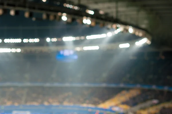 Blurred soccer stadium or ather sport arena at night with projector and stands full of people, fans, crowd