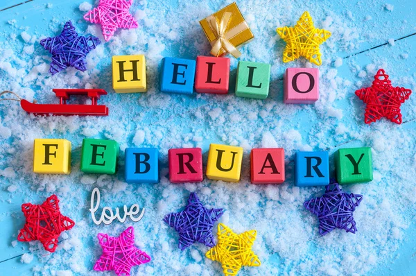 Hello February written on colour wooden toy cubes On light background with snow