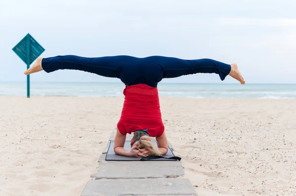 Woman doing yoga asana upavishtha konasana shirshasana, Bound Angle Pose in Head Stand on sea background
