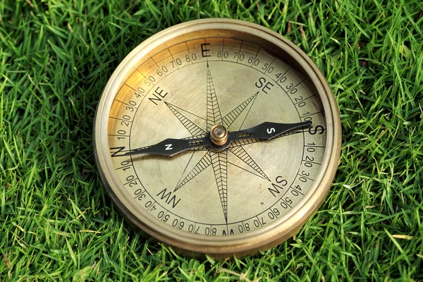 Old directional compass on green grass