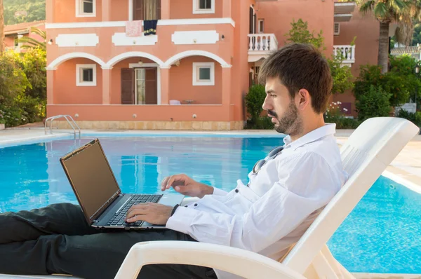 Young bussines man working on his lap top by the pool