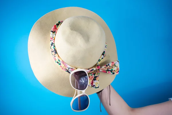 Woman hand holding hat and sunglasses against blue