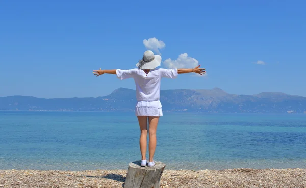 Young woman looking at the mountains above sea with her arms wid