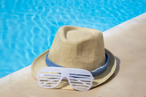 Straw hat and party sunglasses by the pool