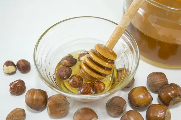 Hazelnuts and honey in  a glass dish next to a jar with honey