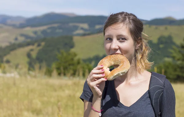 Happy girl hiker eating a doughnut outdoors