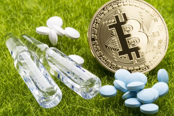 Different pills and ampules with bitcoin coin on the grass background - healthcare cost concept