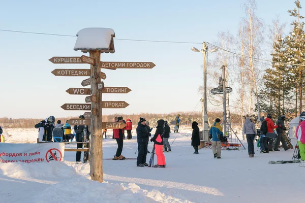 People in ski equipment near a wooden post with direction signs