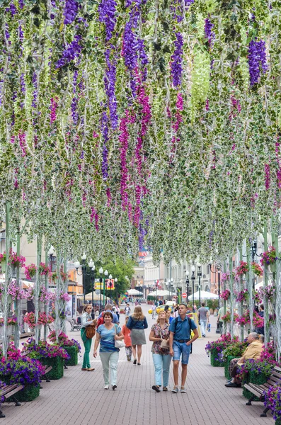 People walk along the avenue, adorned with flowers, hanging vertically