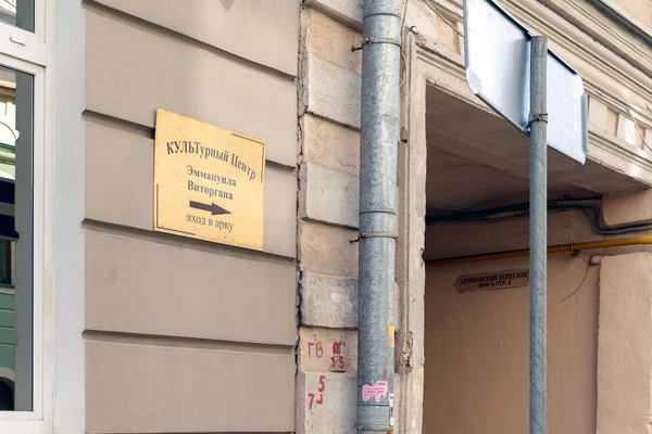 Shiny metal plated tablet hanging on the wall, indicating the direction of the passage to the Cultural Centre Emmanuel Vitorgan