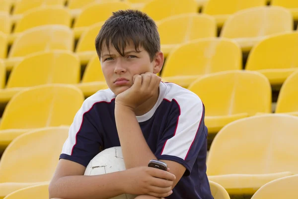 Sad boy with a ball sitting on an empty football grandstand.