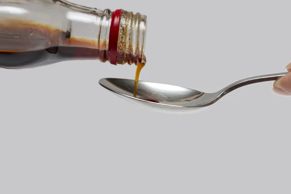 Bottle of cough syrup and a spoon on a white background.
