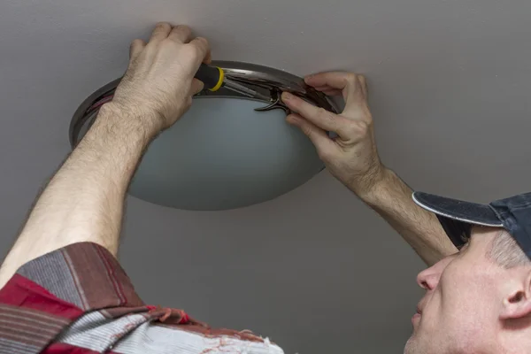 Electrician installs lighting the lamp on the ceiling of the room.