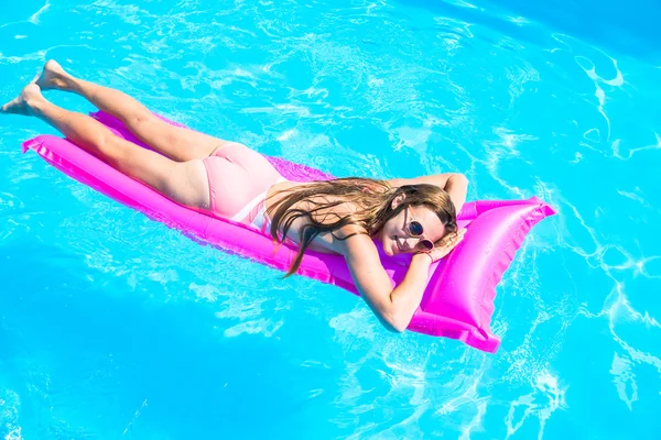The girl floats on an inflatable mattress in the pool