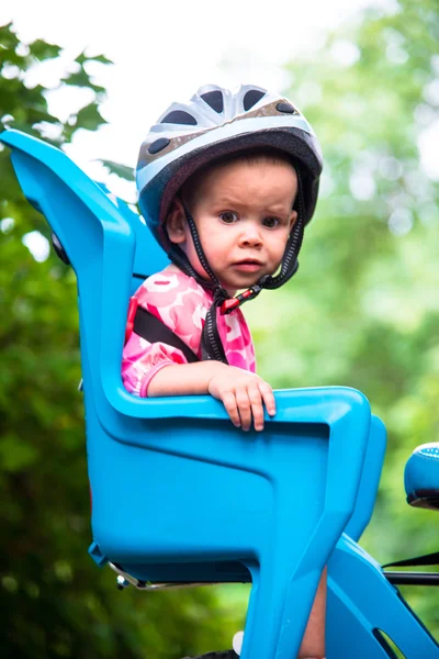 Little girl dressed in bicycle helmet and sits on a bicycle seat