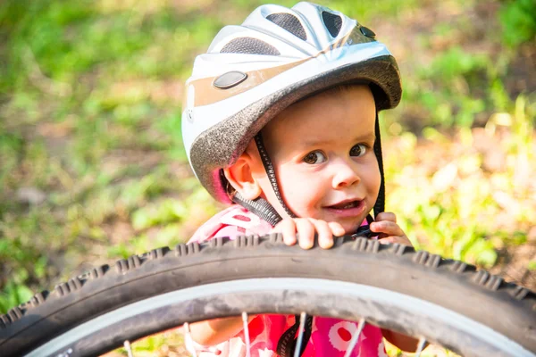 Little girl in a bicycle helmet near a large bicycle wheel