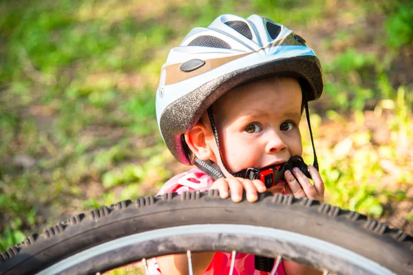 Little girl in a bicycle helmet near a large bicycle wheel