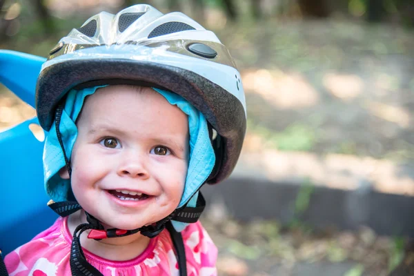 Little girl dressed in bicycle helmet and sits on a bicycle seat