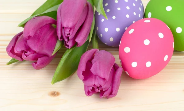 Fresh violet tulips and Easter eggs on a light wooden background with the place for the text.