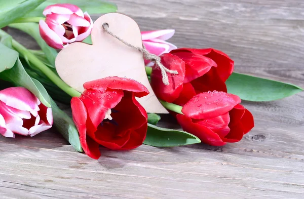 Bouquet of fresh tulips and wooden heart (a place for the text) on a wooden background.