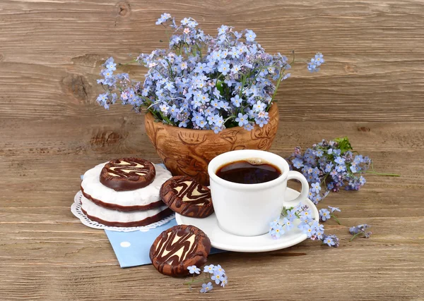 Cup of fresh fragrant coffee with cookies and a bouquet of field forget-me-nots on a wooden background.