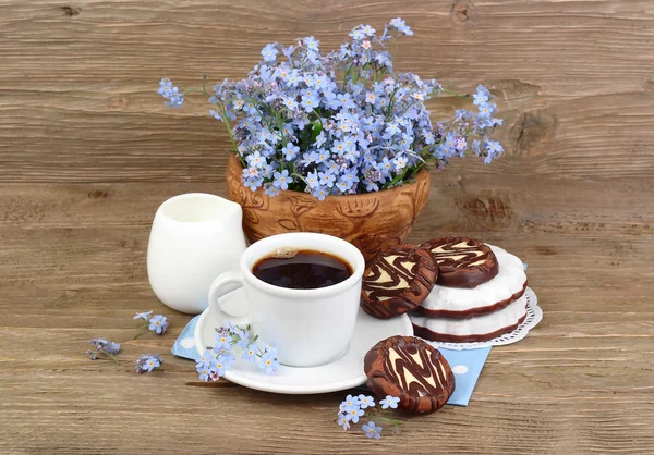 Cup of coffee with cookies and a bouquet of blue wild flowers on a wooden background with a place for the text.