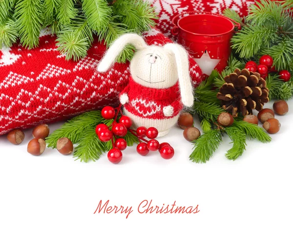 Knitted hare, nuts and cones near knitted pillows and branches of a Christmas tree on a white background. Christmas background.