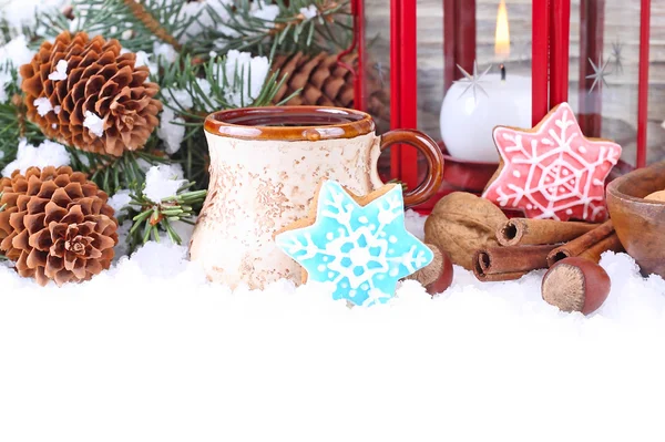 Cup of tea, ginger cookies and nuts near branches of a Christmas tree and cones on snow on a white background. A Christmas background with a place for the text.