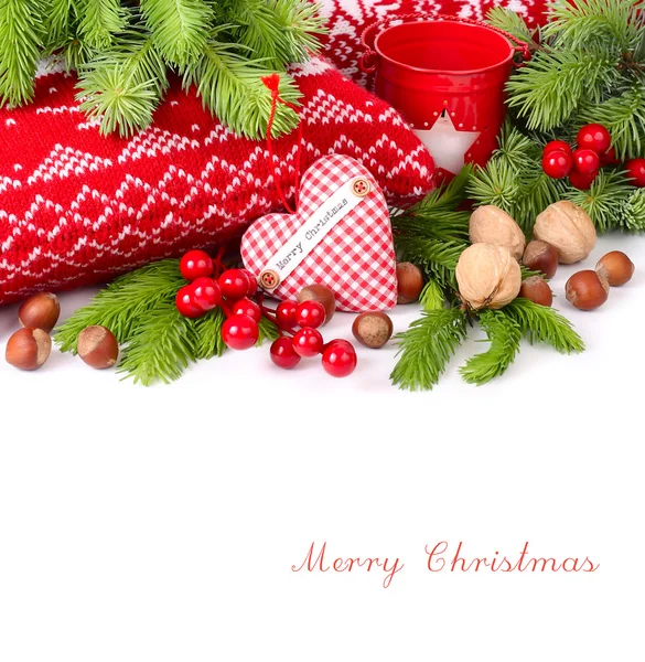 Textile checkered heart, nuts and red berries near knitted pillows and branches of a Christmas tree on a white background. A Christmas background with a place for the text.