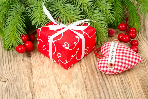 Red gift box, red berries and red checkered textile heart on a wooden background. A Christmas background with a place for the text.