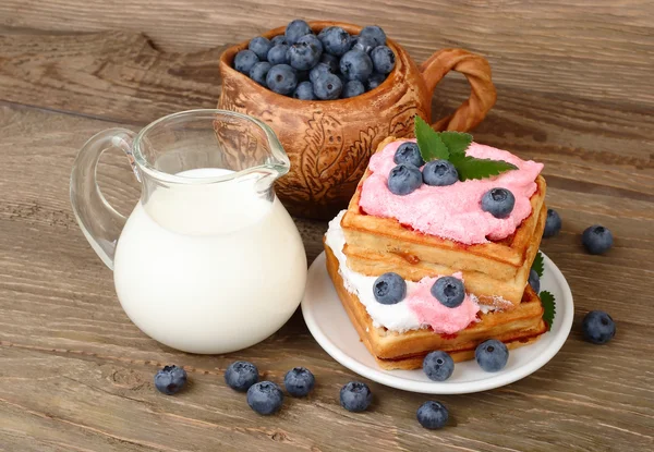 Fresh biscuits with bilberry mousse and blueberry and milk in a transparent jug on a wooden background.