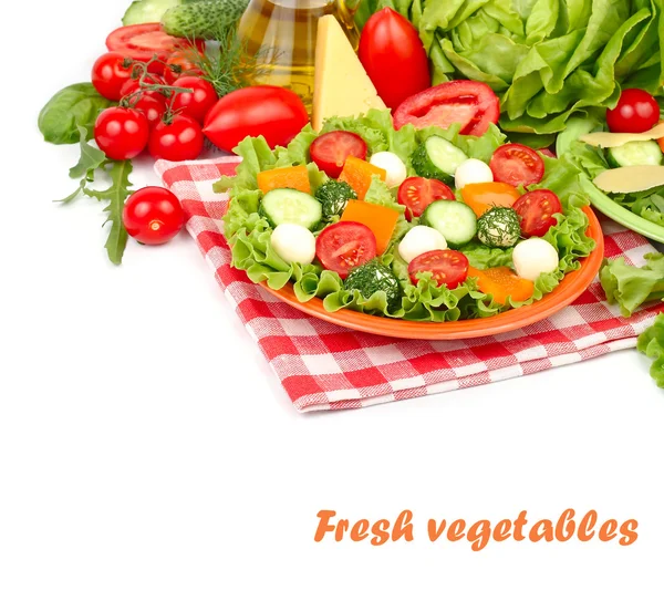 The Greek salad with cheese balls on an orange plate on a red checkered napkin and fresh ripe vegetables and herbs on a white background with a place for the text.