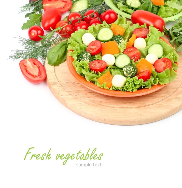 The Greek salad with cheese balls and fresh ripe vegetables and herbs on an orange plate on a white background with a place for the text.