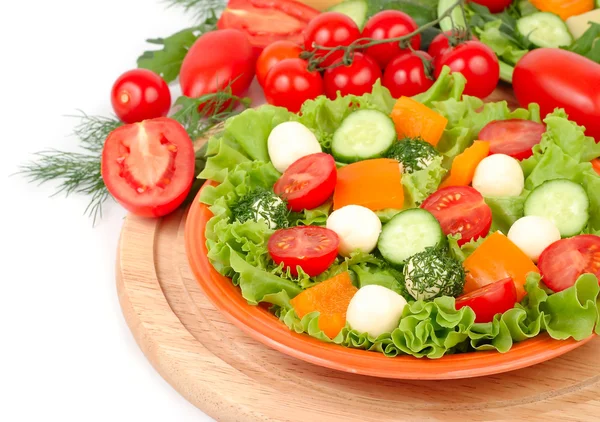 The Greek salad with cheese balls on an orange plate and fresh ripe vegetables and herbs on a white background with a place for the text.