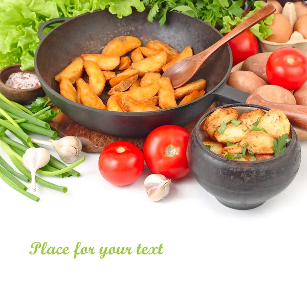 Fried potatoes in a black pig-iron frying pan and fresh vegetables on a white background with a place for the text.