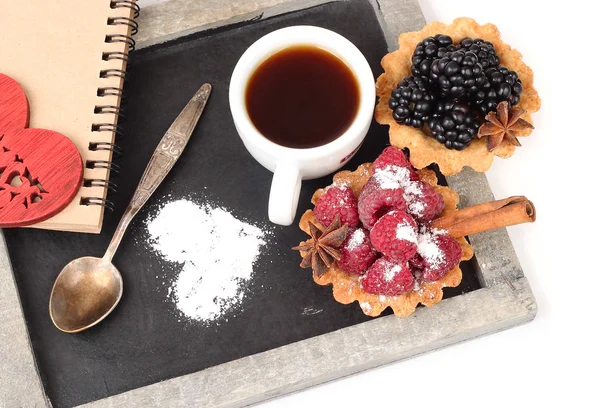 Baskets from shortcake dough with blackberry and raspberry and a cup of coffee on a cretaceous board on a white background with a place for the text.