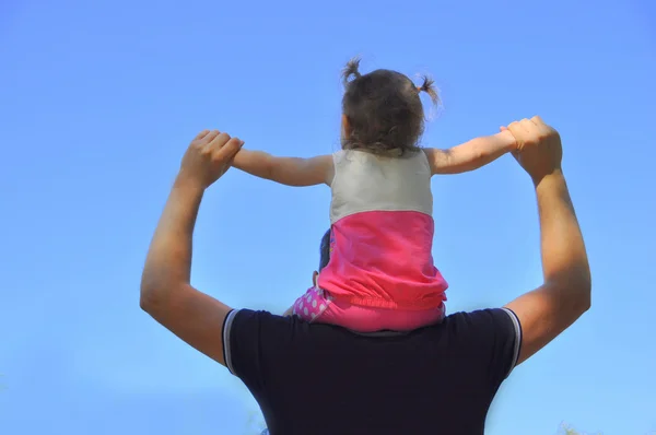 Little girl sitting on the shoulders of the  father