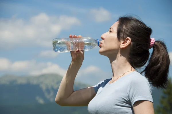 Girl  drinks water from a bottle on the background the mountains