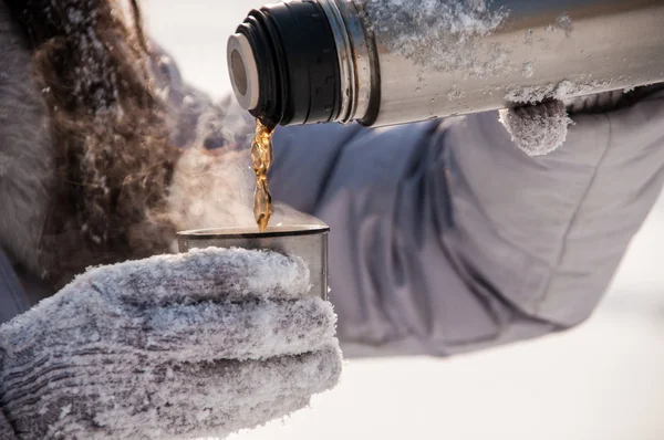 Woman pours tea from a thermos winter